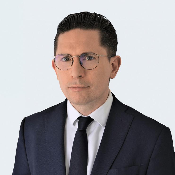 Daniel Pohl, LL.M., ein Mann mit Brille und zurückgekämmtem Haar, trägt einen dunkelblauen Anzug, ein weißes Hemd und eine dunkle Krawatte. Er blickt ernst in die Kamera vor hellem Hintergrund.