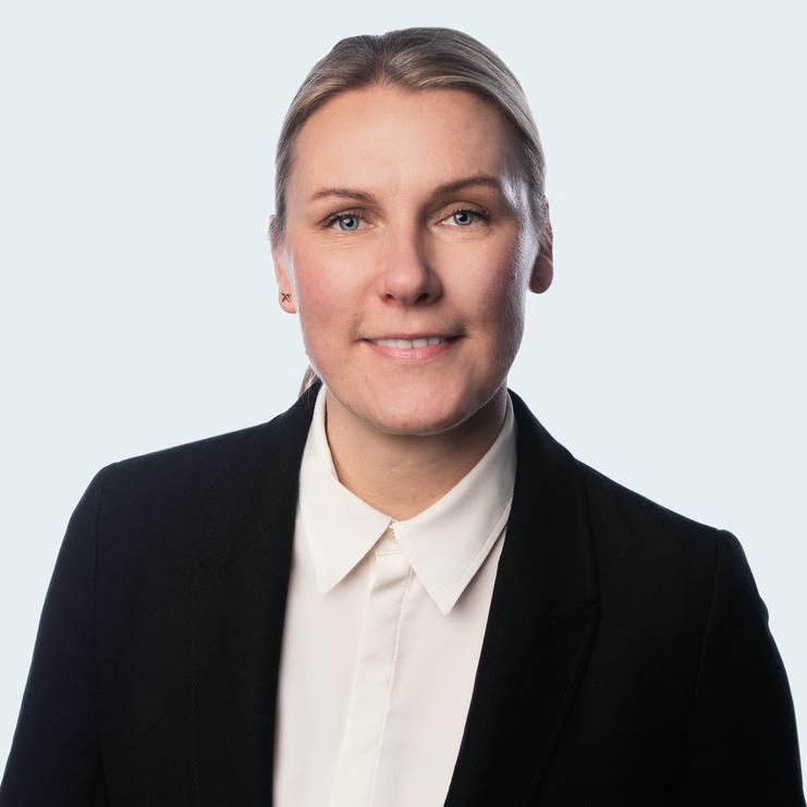 Katja Goldbach, LL.M., eine Frau mit blondem Haar, trägt einen schwarzen Blazer über einer weißen Bluse. Sie lächelt freundlich und blickt direkt in die Kamera vor einem hellen Hintergrund.