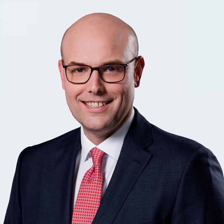 Matthias Kleffner, LL.M., ein Mann mit Brille und Glatze, trägt einen dunklen Anzug, ein weißes Hemd und eine rote Krawatte. Er lächelt freundlich in die Kamera vor einem hellen Hintergrund.